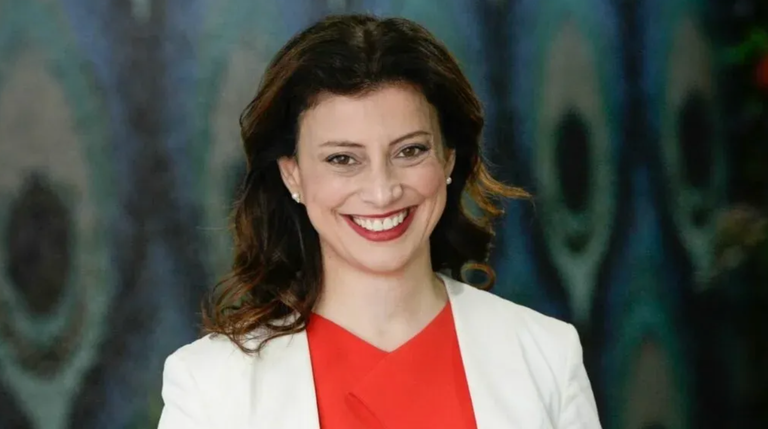 South Australian politician Andrea Michaels MP smiling in a portrait photo while wearing a white blazer over a red top.